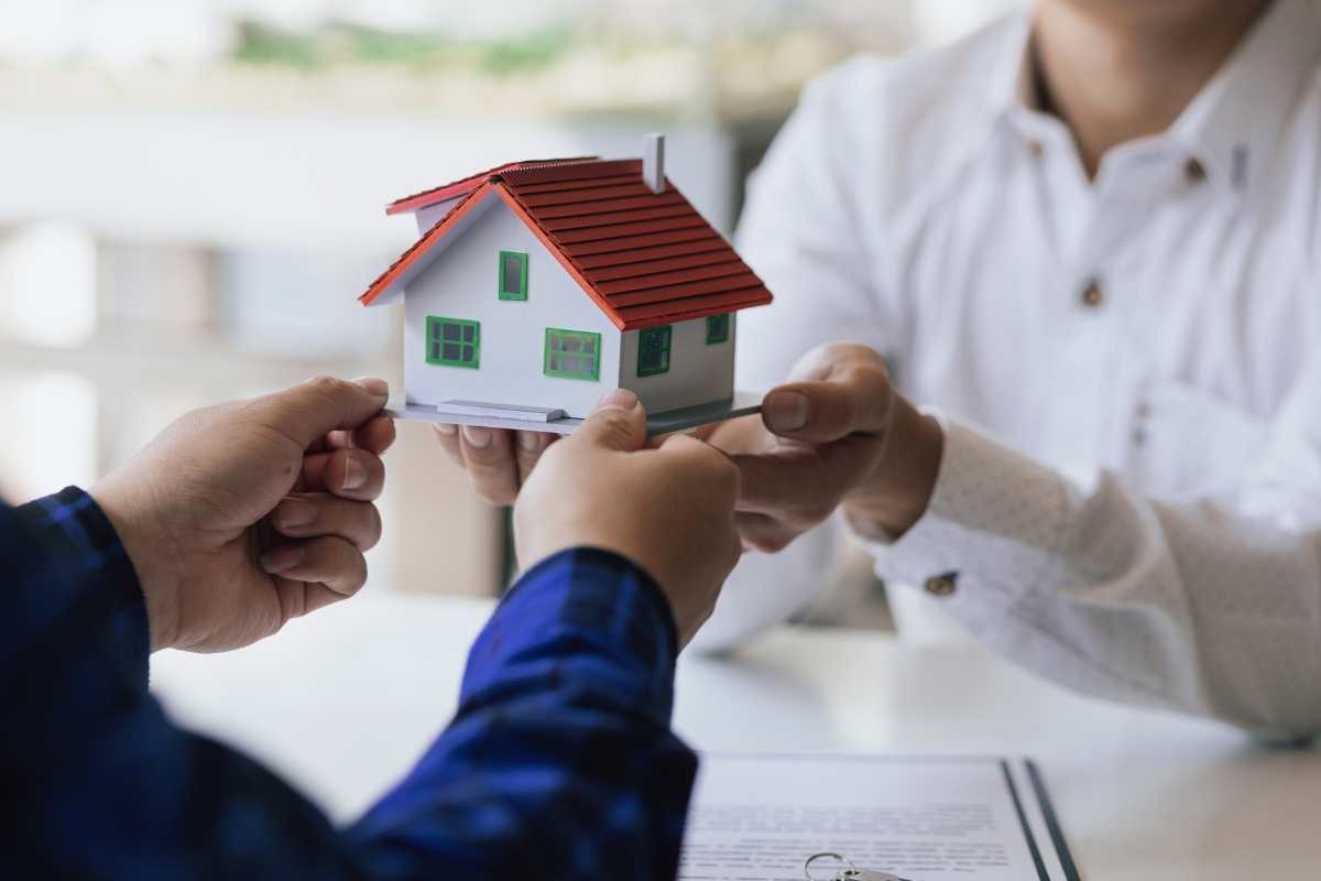 persona con in mano una casa in miniatura