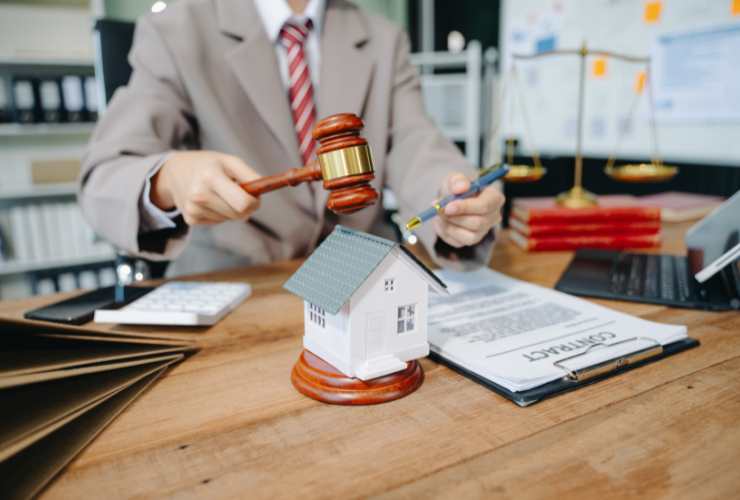 scrivania con casa in miniatura, documenti e persona con martello del giudice